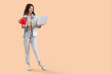 Fototapeta premium Young woman with gift and laptop video chatting with boyfriend on beige background. Online dating