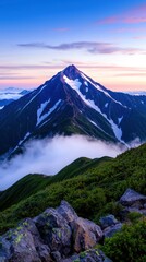 Majestic mountain peak at sunrise, clouds below, green slopes, rocky foreground.