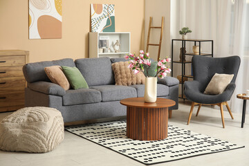 Sofa, armchair and blooming magnolia branches in vase on coffee table in interior of living room