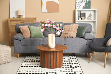 Sofa and blooming magnolia branches in vase on coffee table in interior of living room