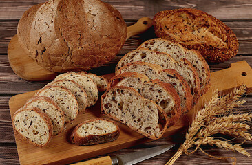Freshly baked whole grain homemade sourdough bread with crispy crust, sliced and ears of wheat on wooden table, modern baking concept, healthy natural food