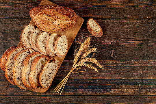 Freshly baked whole grain homemade sourdough bread with crispy crust, sliced and ears of wheat on wooden table, modern baking concept, healthy natural food