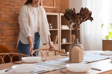 Vase with dried flowers and dishes on dining table in room, closeup