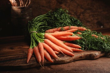 Vibrant carrots with lush green tops are arranged on a rustic wooden board, celebrating the essence...