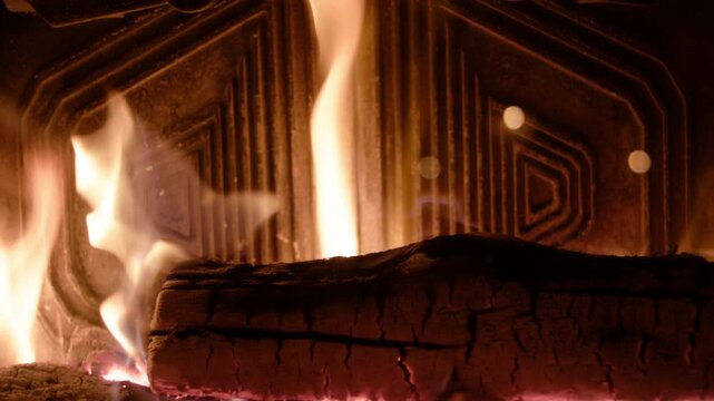 In the fireplace, flames sway against geometric metal panels with concentric shapes. A slowly charring log reveals glowing embers in its cracks, creating depth and mesmerizing warmth.