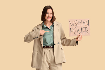 Beautiful young woman pointing at WOMAN POWER sign on beige background. Women's history month