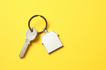Metallic key with keychain in shape of house on color background