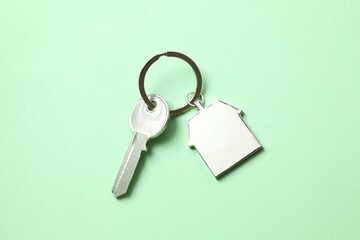 Metallic key with keychain in shape of house on color background