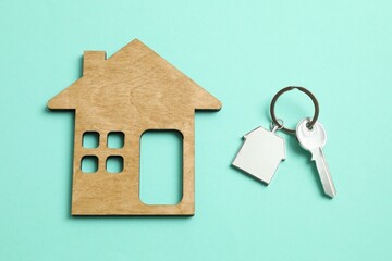 Metallic key with keychain and wooden house on color background