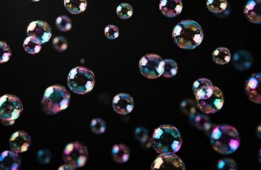Floating soap bubbles shine with rainbow color against black. Round shapes create abstract design. Liquid sphere reflects light with iridescent shades. Magic wallpaper for party mood background.