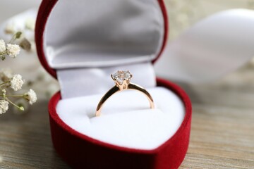 Beautiful shiny gold engagement ring with large diamond gemstone in a rich red velvet box on the...