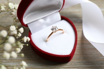 Beautiful shiny gold engagement ring with large diamond gemstone in a rich red velvet box on the...