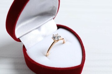 Beautiful shiny gold engagement ring with large diamond gemstone in a rich red velvet box on silk...