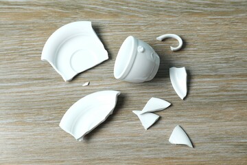 White cup and plate broken on wooden background