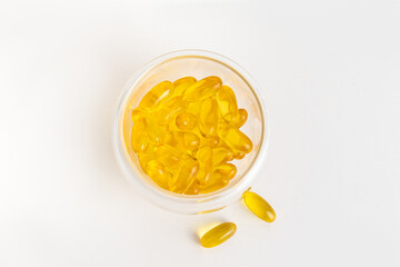 Yellow vitamin capsules in glass bowl on white background. Top view