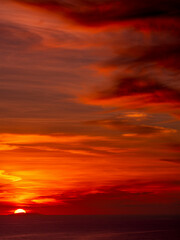Dramatic sky of clouds reflecting strong hues of orange, pink, blue and yellow lighting up and reflecting off of the horizon of the Pacific Ocean 