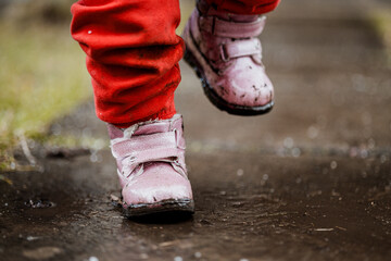 little girl in pink boots dancing and jumping on wet asphalt in rain and snow, girl in the rain,...