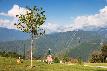 A girl stands in a park with a tree in the background and looks into the distance