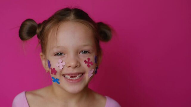 A funny preschool-age girl without upper front teeth decorated her face with paper puzzle pieces - a common symbol of autism