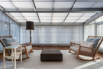 Cozy terrace with wooden rocking chairs. Light curtains on the glass roof and panoramic windows.
