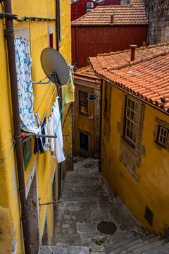 A cozy street that leads down to Porto, with a yellow house on the right and an orange house with orange roofs on the left