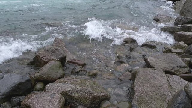 Waves crash against dark stones on the coast, close up