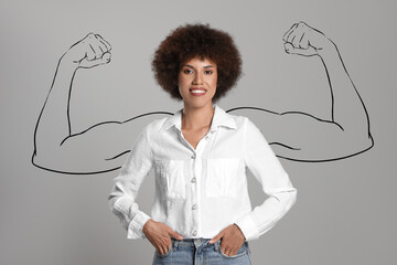 Confident beautiful woman with drawing of strong arms behind her on grey background