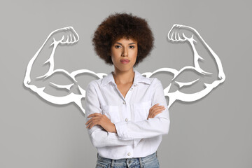 Confident beautiful woman with drawing of strong arms behind her on grey background