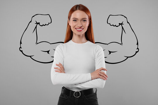 Confident beautiful woman with drawing of strong arms behind her on grey background