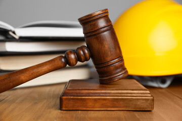 Accident at work concept. Gavel, books and construction worker's protective gear on wooden table, selective focus