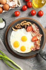 Tasty fried eggs with bacon and mushrooms served on grey table, flat lay