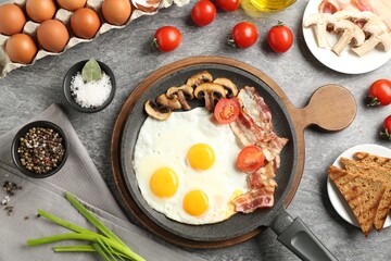 Tasty fried eggs with bacon and mushrooms served on grey table, flat lay
