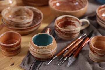 Different beautiful pottery and set of clay crafting tools on wooden table, closeup