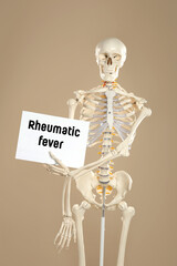 Rheumatism. Artificial human skeleton model holding paper with Rheumatic Fever words on dark beige...