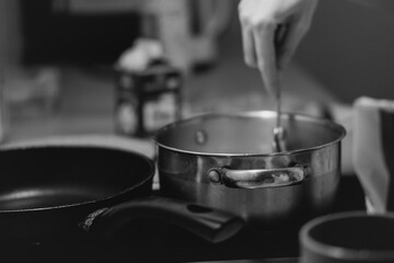 A close-up shot of a hand stirring food in a stainless steel pot on a stovetop, with a blurred...