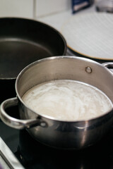 A close-up shot of a hand stirring food in a stainless steel pot on a stovetop, with a blurred...