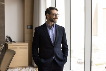 Pensive middle-aged Portuguese businessman posing in boardroom, dressed in suit, look into distance...