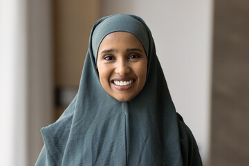 Head shot close up portrait of beautiful self-assured Middle Eastern business woman dressed in traditional hijab attire smile look at camera indoors, exuding independence, professional achievements