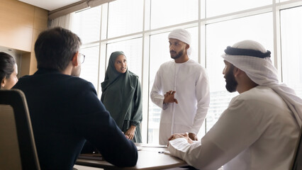 Arabian business partners negotiate gather in conference room, listening speech, offer or ideas of team leader, make presentation, exudes leadership and authority. Multicultural business meeting event