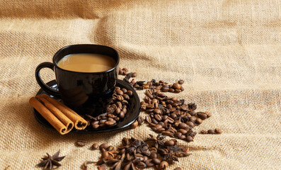 A black cup with a saucer and coffee and coffee beans on a brown cloth background