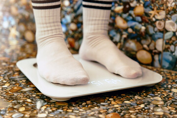 Close-up of legs in white socks standing on digital floor scales. The concept of achieving weight loss. Feet standing on floor scales in the bathroom