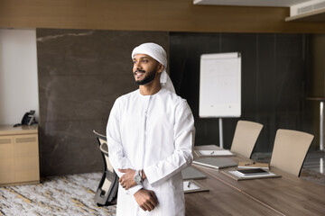 Confident businessman dressed in traditional dishdasha standing in board room, looking aside with thoughtful expression, take break between meetings, thinks about future opportunities and achievements