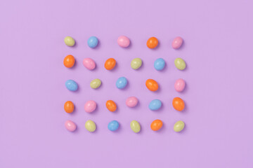 Colorful easter dragee on a violet background. Multicolored candies in the shape of eggs covered with glaze