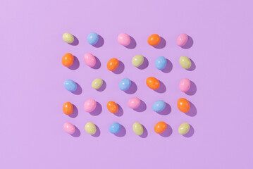 Colorful easter dragee on a violet background. Multicolored candies in the shape of eggs covered with glaze