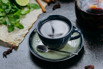 Aromatic herbal tea with cinnamon, mint, lime, and hibiscus in a stylish teapot and cup setting
