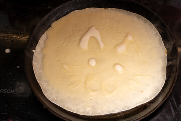 Creative crepe in a pan resembling a cat's face, with ears, eyes, nose, and whiskers.