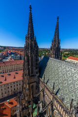 Obraz premium A high-angle shot showcasing the spires of a gothic cathedral rising above a cityscape with red-roofed buildings under a bright blue sky