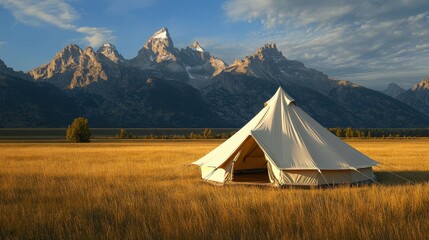 Scenic Tent Camp in Golden Meadow with Majestic Mountain Range Under a Bright Blue Sky