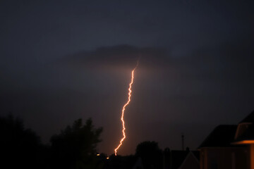 Dramatic lightning strike against a dark stormy sky with glowing orange light trails across the horizon, capturing raw power and atmospheric intensity