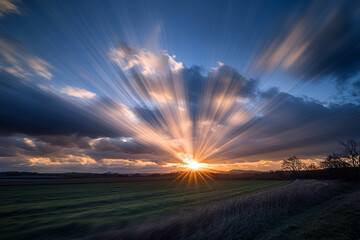 Dramatic sunset with radiant sunbeams piercing through clouds over an open field, creating a breathtaking natural landscape